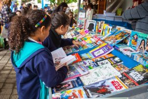 Na imagem é possível ver crianças em um estande de livros em uma festa literária internacional, como será a Fiflio